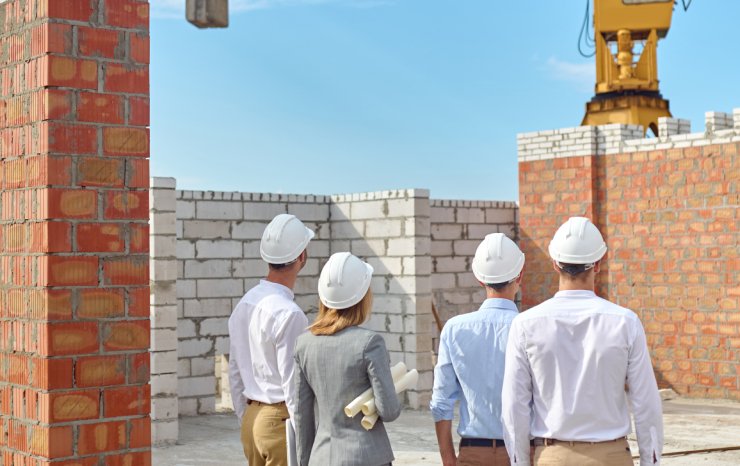 Four people in protective helmets inspecting the building area